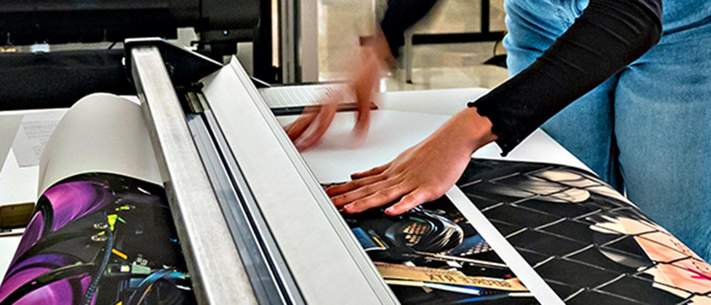 Cutting a large sheet of paper covered in printed artwork.