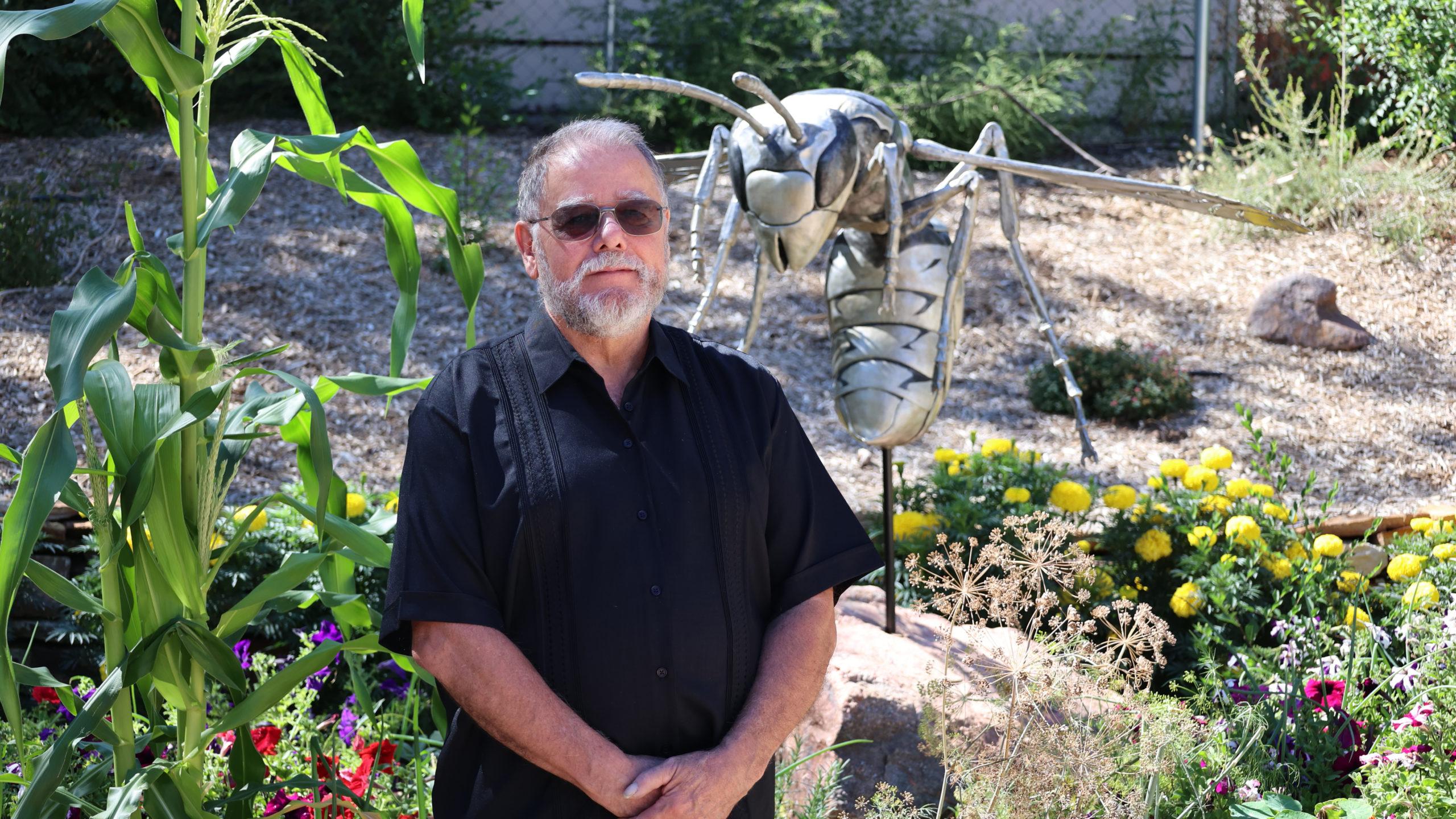 John Montaña standing in front of a piece of artwork, a metal sculpture of a wasp